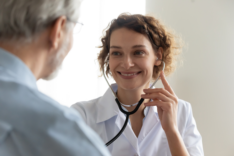 Close up of a smiling doctor using a stethoscope to examine a mature patients heart rate in clinic.