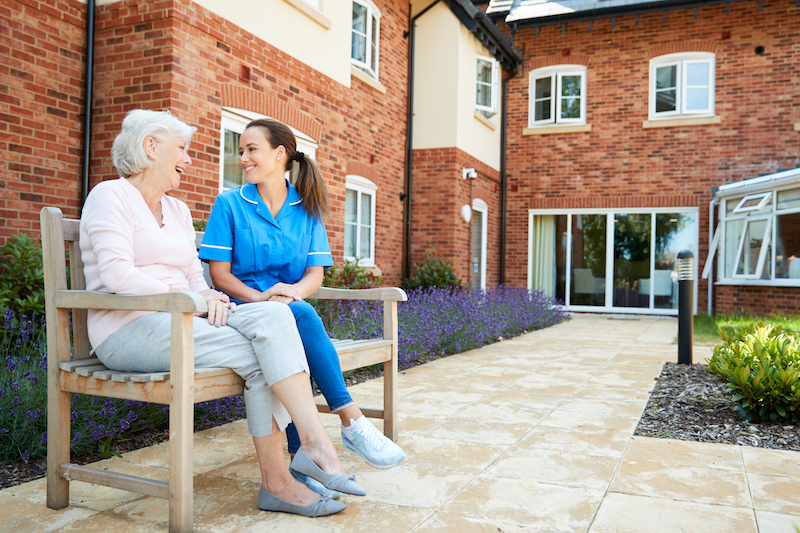 Senior Woman Sitting On Bench And Talking With Nurse