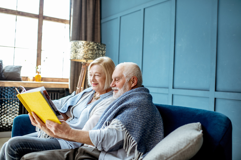 two seniors reading a book on a couch.