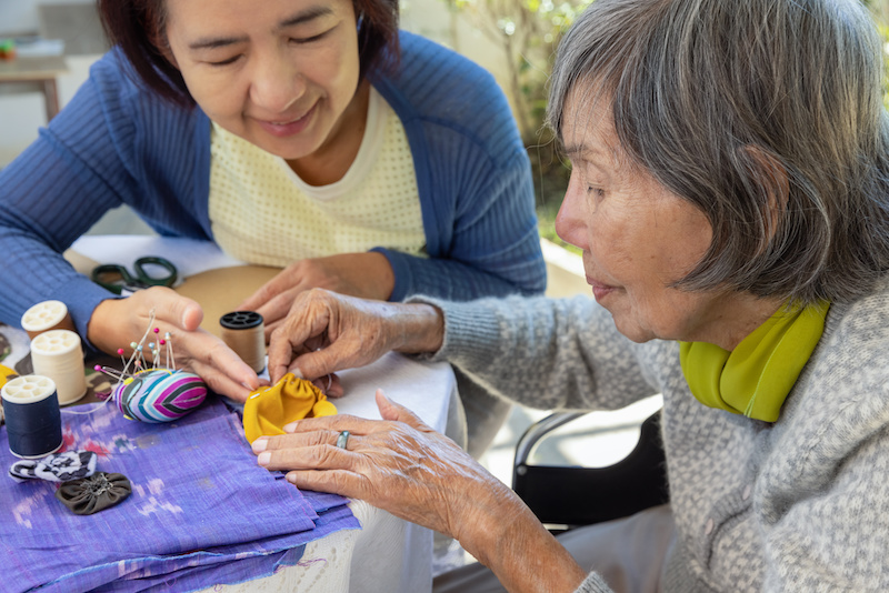 Elderly woman and daughter working on needle crafts at senior living