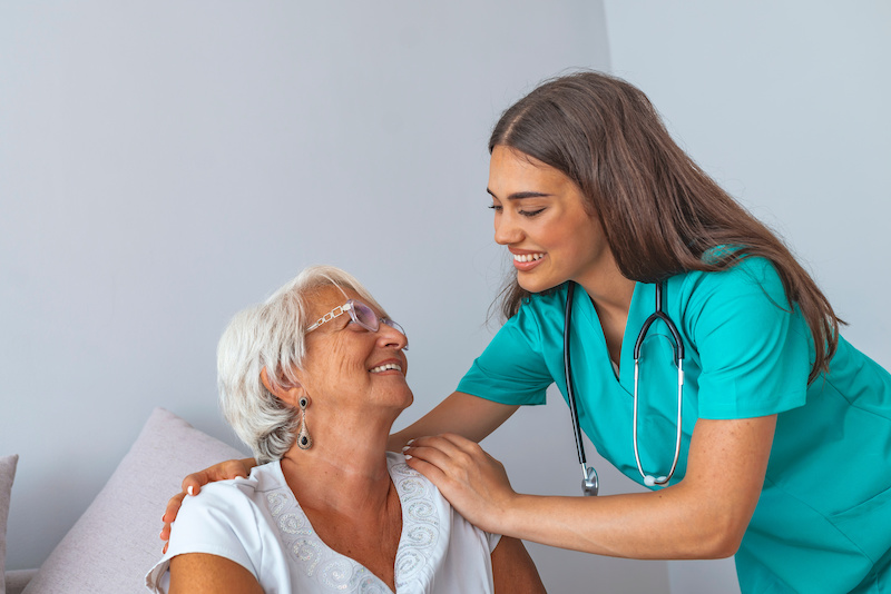 Professional helpful caregiver comforting smiling senior woman at nursing home