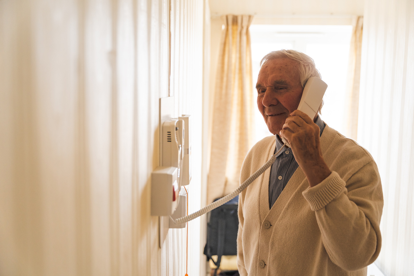 Happy old man speaking on the phone, slightly straining. This could be due to his struggle to remember something.