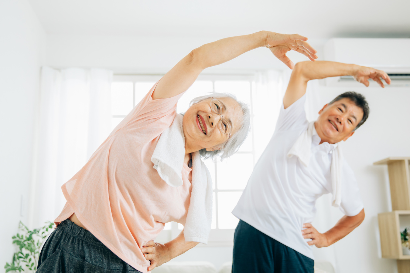 An elderly couple (woman on the left, man on the right) performing an upper body stretch.