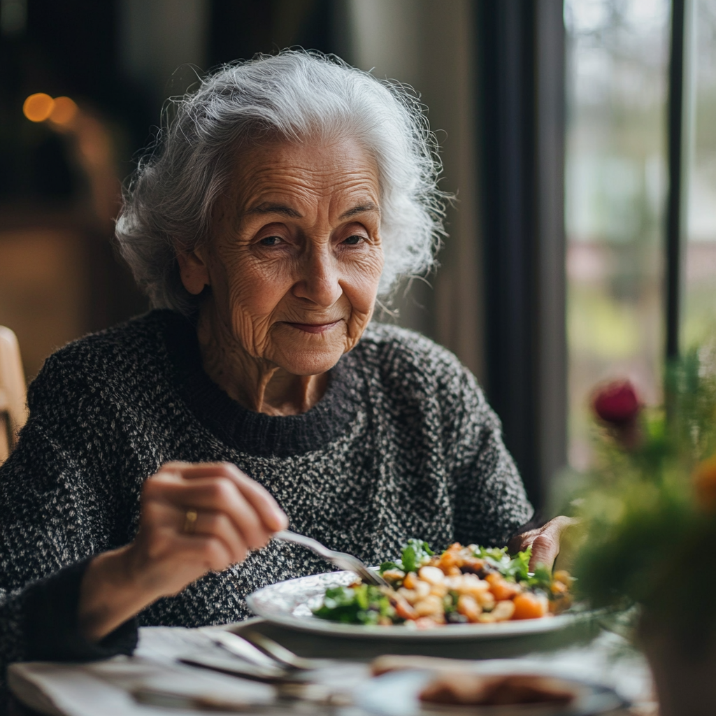 An older woman sitting at a table holding a fork over her plate. She has a serene look on her face. An example of mindful eating.